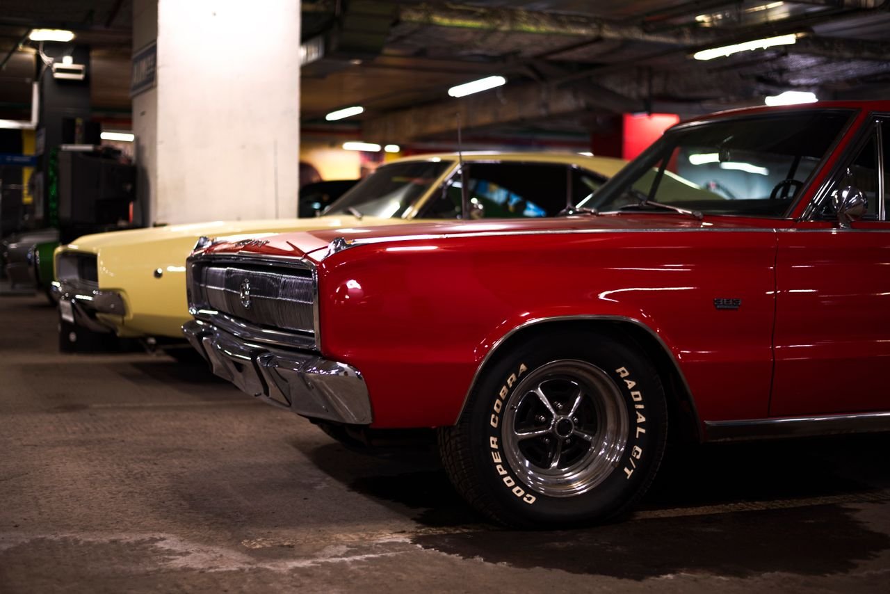 Close-up of vintage muscle cars with red livery parked in an indoor garage.