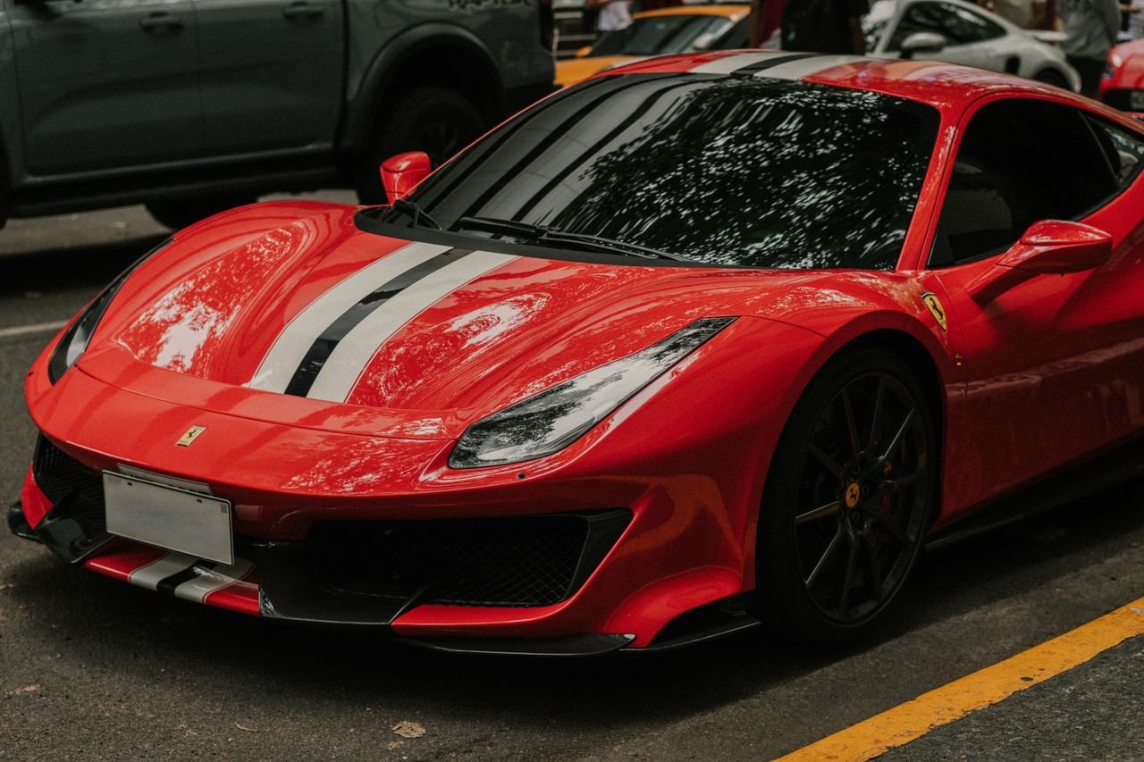 A sleek red Ferrari sports car with racing stripes parked outdoors, showcasing luxury and speed.
